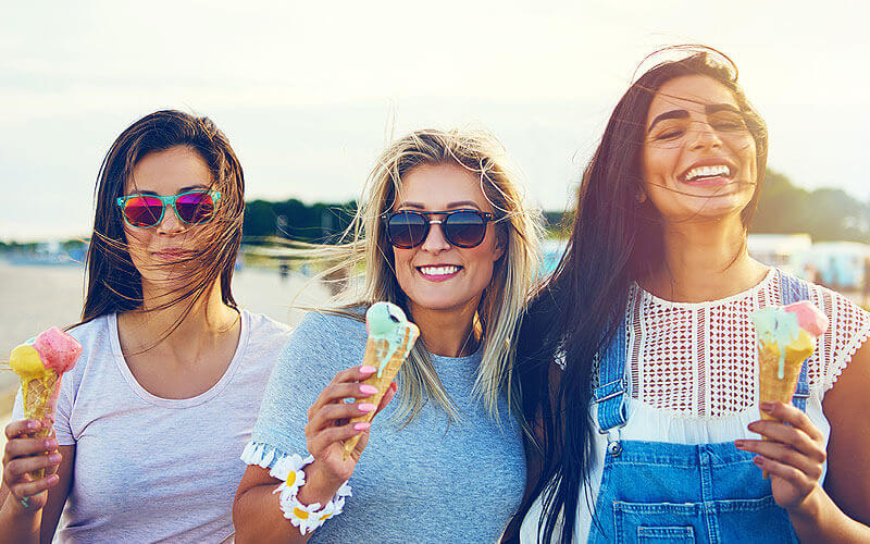 A group of three young women, holding ice cream cones, smiling while outside