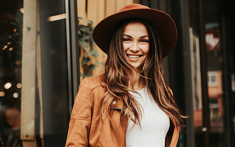 Smiling young woman, wearing a brown hat and a brown leather coat with a white shirt